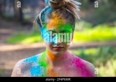 Junge attraktive Frau auf dem Holi Farbe Festival der Farben im Park. Spaß im Freien. Mehrfarbige Puder färbt das Gesicht. Nahaufnahme im Hochformat. Stockfoto