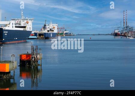 Ein Blick auf Dublin Port, Irland, mit Schiffen auf der linken Seite, die Poolbeg Towers auf der rechten Seite und der Poolbeg Leuchtturm in der Ferne. Stockfoto