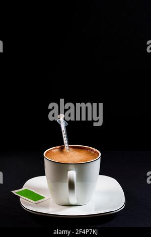 Kaffee mit Milch in Porzellanbecher mit Spritze in der Kaffee.Dies ist ein Portrait-Format Foto gegen einen schwarzen gemacht Hintergrund unter künstlichem Lig Stockfoto