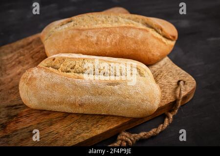 Rustikale Brötchen auf Holzschneidebrett auf dunklem Tisch Stockfoto