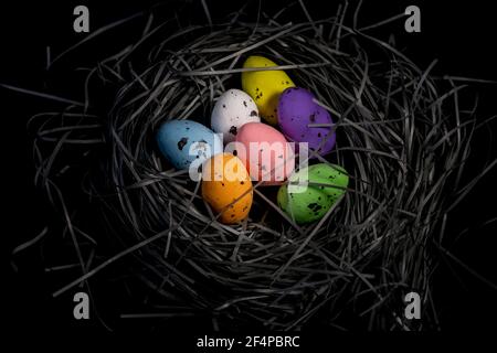 Bunte Eier in einem handgefertigten Korb auf schwarzem Hintergrund. Kreativer östlicher Hintergrund Stockfoto