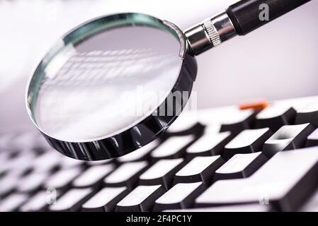 Lupe auf den Tasten einer schwarzen Computertastatur. Stockfoto