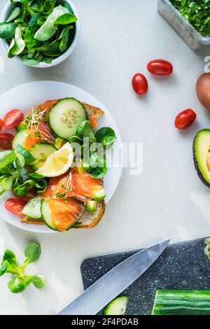 Draufsicht gesundes Sandwich mit Gemüse, Lachs und Grün auf dem Tisch mit Zutaten.geröstetes Brot mit Avocado, Lachs, mikrogrünen Sprossen Stockfoto