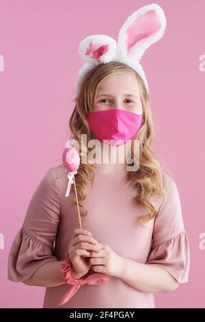 Frohe Ostern. modernes Kind in rosa Kleid mit rosa Maske, Hasenohren und osterei isoliert auf rosa. Stockfoto