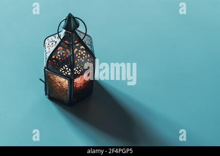 Alte arabische Laterne aus Metall mit farbenfrohem Glasdekor mit langem Schatten. Blau türkisfarbener Tischhintergrund. Karmonat Ramadan Grußkarte, Einladung Stockfoto