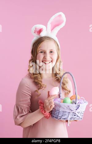 Happy stilvolle Mädchen in rosa Kleid mit Hasen Ohren und Korb von ostereiern vor rosa Hintergrund. Stockfoto