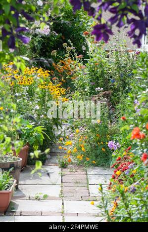 Eine hübsche und farbenfrohe Nahaufnahme eines privaten britischen Cottage-Stil Sommergarten Grenze in voller Blüte mit Blumen auf den Weg überfließen. Stockfoto