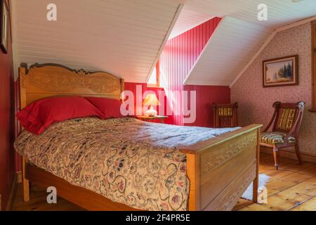 Doppelbett auf Ulmenholz-Rahmen mit gepressten Designelementen auf Kopfteil und Fußteil, Nachttisch aus Ahornholz, gepolsterte Sessel im viktorianischen Stil Stockfoto