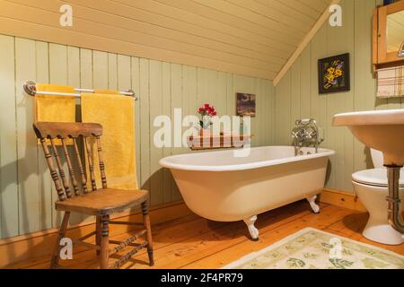 Freistehende Roll Top Klaue Fuß Badewanne und antiken Stuhl aus Holz In grün und beige bemalte Holzdiele Badezimmer mit Eastern hemlock Dielen Stockfoto