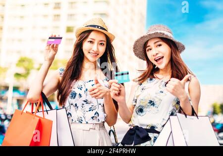 Schöne Mädchen halten Einkaufstaschen und zeigen Kreditkarte mit Daumen hoch Stockfoto