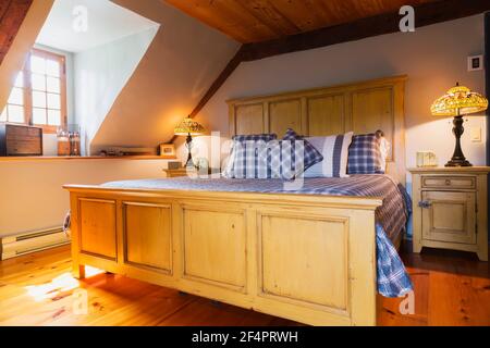 Kingsize-Bett mit Kopfteil und Fußteil aus Buttermilch-Kiefernholz, blau, weiß und rot tartanischem Bettüberwurf und antiken Nachttischen aus Holz mit tiffany-Lampe Stockfoto