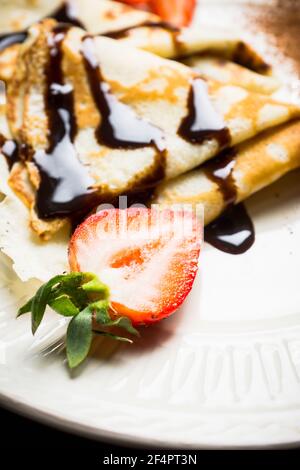 Russische dünne Pfannkuchen (Blini), mit Erdbeer- und Schokoladensoße. Selektiver Fokus. Stockfoto