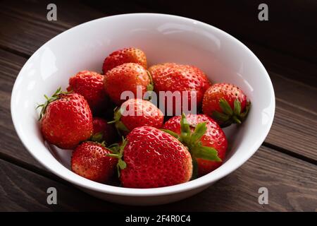 Natürliche reife Erdbeeren in einer schlichten weißen Schale auf einem dunklen Holztisch Stockfoto