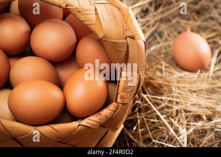 Frische braune Hühnereier in einem Korb und im Nest aus Heu in einer Scheune Stockfoto