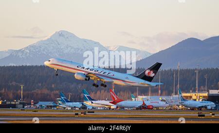 Richmond, British Columbia, Kanada. März 2021, 22nd. Ein Cargojet Boeing 757 Air Cargo Jet (C-FKAJ) hebt bei Sonnenuntergang vom Vancouver International Airport ab. Im Hintergrund parkten die Flugzeuge WestJet und Sunwing Boeing 737 am Inlandsterminal des Flughafens. Quelle: Bayne Stanley/ZUMA Wire/Alamy Live News Stockfoto