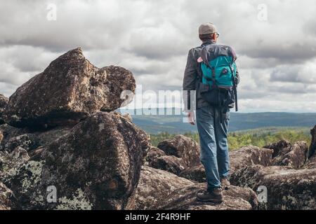 Ein Tourist mit Rucksack steht auf dem Gipfel des Berges und genießt die Aussicht von oben. Das Konzept des Sports und des aktiven Lebens. Stockfoto