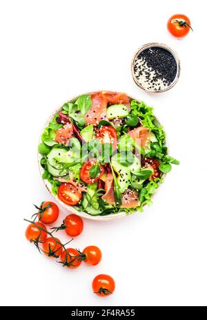 Frischer Salat mit gesalzenem Lachs, Avocado, Gurke, Sesam, Olivenöl, Tomaten und gemischte Kräuter. Weißer Hintergrund, Draufsicht, Kopierbereich Stockfoto