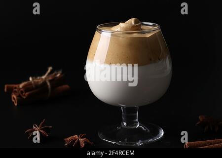 Dalgona cremiger Kaffee in einem Glas auf schwarzem Hintergrund mit Schlagschaum. Koreanischer Kaffeetrend. Nahaufnahme Stockfoto