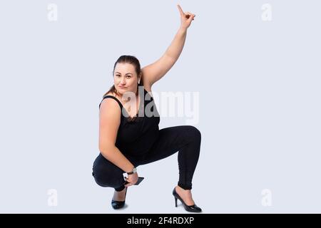 Junge und große kaukasische Geschäftsfrau trägt Schuhe mit Absätzen, tanzt und hat Spaß auf grauem Hintergrund, hören Sie die Musik auf dem Smartphone und Stockfoto