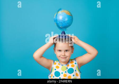 Mädchen in einem weißen Sommerkleid hält einen Globus auf dem Kopf wie ein Hut, lenkt die Aufmerksamkeit auf Umweltprobleme, isoliert auf einem blauen Hintergrund Stockfoto