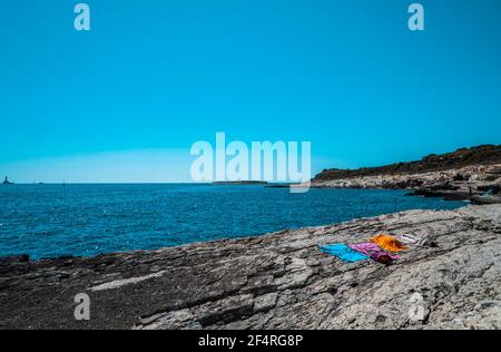 Handtücher und Menschen am Steinstrand im Nationalpark Kamenjak, Istrien, Kroatien Stockfoto