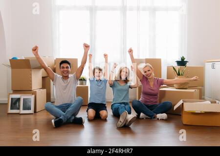 Kaukasische Familie Gruppe von vier Putting Hände bis für den Erfolg in Bewegung in Tag. Vater, Mutter, Tochter und Sohn helfen beim Entladen von Sachen aus Kisten. Stockfoto