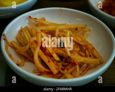 Orange eingelegter Rettich in einer weißen Tasse zum Essen. Asiatische Beilage eingelegter Rettich, koreanische Küche traditionell. Kein Fokus, speziell. Stockfoto