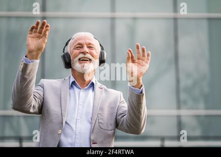 Porträt eines Geschäftsmannes im Freien, der Musik über Kopfhörer genießt. Stockfoto