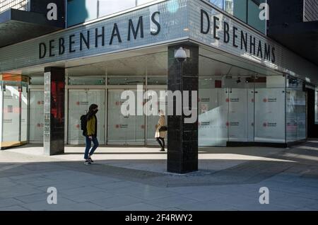 London, Großbritannien - 26. Februar 2021: Zwei Fußgänger, die jeweils Gesichtsmasken tragen, gehen an den verschlossenen Türen des mittlerweile verschlossenen Flagship-Stores der Debenh vorbei Stockfoto