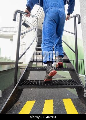 Arbeiter auf der Treppe. Low-Angle-Ansicht des Industrietechnikers, der in einer Fabrik auf Stahltreppen klettert. Stockfoto