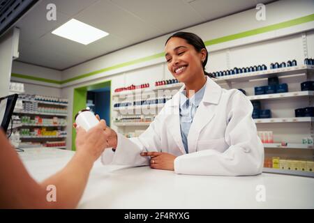 Junge Frau, die in der Apotheke gibt Flasche Pillen zu Kunde Stockfoto