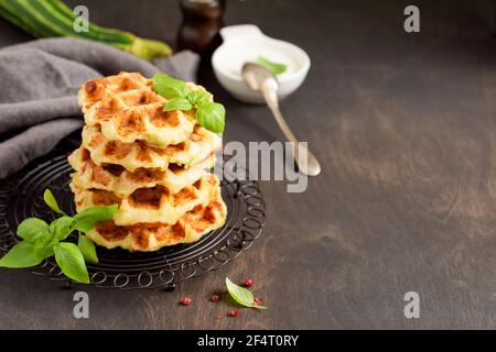 Hausgemachte Zucchini Waffeln Stapel mit Käse, Sause und Blatt Basilikum auf alten Holz dunklen Hintergrund. Konzept der Keto Ernährung Lebensmittel. Selektiver Fokus Stockfoto