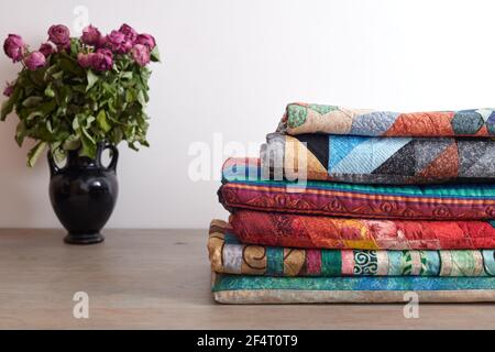 Quilts Stapel und ein Bouquet von getrockneten Rosen in einem Vase auf weißem Wandhintergrund Stockfoto