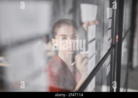 Porträt der jungen Geschäftsfrau schreiben auf Glaswand während der Planung Projekt im modernen Büro, kopieren Raum Stockfoto