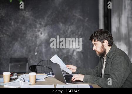 Seitenansicht Porträt von modernen bärtigen Geschäftsmann lesen Dokumente am Tisch, während die Arbeit in schwarz minimal Büro, Kopierer Platz Stockfoto