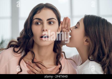 Tochter erzählt Geheimnis zu Mutter im Flüstern im Ohr Stockfoto