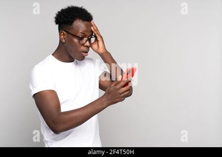 Nachdenklicher schwarzer Mann kratzt Kopf, Blick auf Handy, Denken, plant oder überdenkt etwas Stockfoto