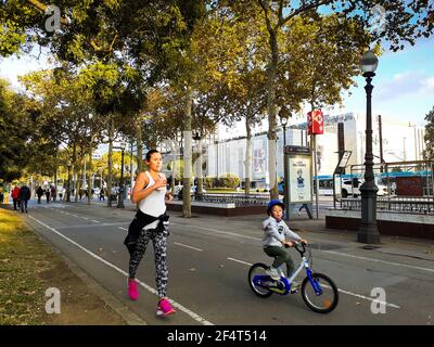 Mutter und Sohn beim Sport. Eine Mutter, die läuft, während ihr kleiner Sohn auf einer Fahrradstraße in der Stadt Fahrrad fährt. Stockfoto