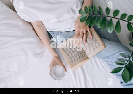 Junge Frau in legerer Kleidung liest ein Buch und hält Ein Glas Wasser Blick von oben Stockfoto