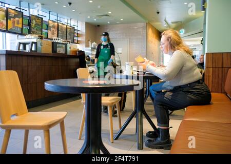 Moskau. Russland. März 23, 2021. Eine Frau sitzt an einem Tisch in einem Café und hält ein Smartphone. Es gibt eine Papiertasse Kaffee auf dem Tisch. Im Stockfoto