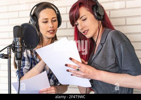 Junge Frauen in Kopfhörern sprechen über Drehbuch, während sie in der Nähe stehen Mikrofon vor Radiosendung im Studio Stockfoto