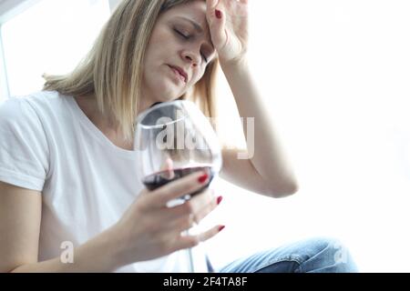 Müde Frau mit einem Glas Rotwein hält ihren Kopf Stockfoto