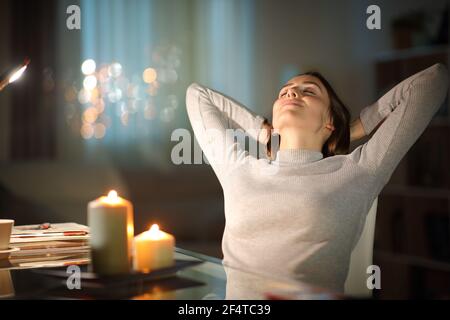 Entspannte Frau, die in der Nacht auf einem Stuhl sitzt Mit Kerzen zu Hause Stockfoto