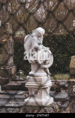 Alter Friedhof mit Trauerengel auf dem Grab mit Kranz mit Wort Souvenir (Erinnerung auf Französisch) durch Zaun gesehen. Frankreich. Trauer, Verlust, Traurigkeit. Stockfoto