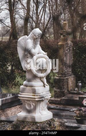 Alter Friedhof mit Trauerengel auf dem Grab mit Kranz mit Wort Souvenir (Erinnerung auf Französisch) durch Zaun gesehen. Frankreich. Trauer, Verlust, Traurigkeit. Stockfoto