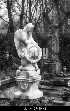 Alter Friedhof mit Trauerengel auf dem Grab mit Kranz mit Wort Souvenir (Erinnerung auf Französisch) durch Zaun gesehen. Frankreich. Trauer. Schwarzweißfoto Stockfoto