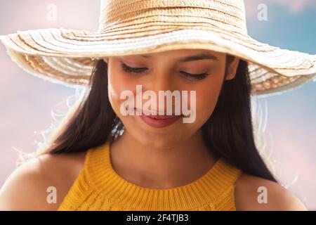 EINE GLÜCKLICHE FRAU TRÄGT SOMMERHUT UND SCHAUT NACH UNTEN UND LÄCHELT Stockfoto