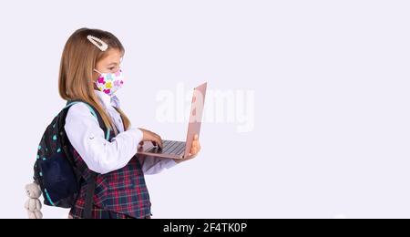 Banner. Schülerin in einer Schutzmaske und einem Laptop-Computer auf einem grauen Studio-Hintergrund mit Seitenraum. Fernunterricht während einer Pandemie. Stockfoto