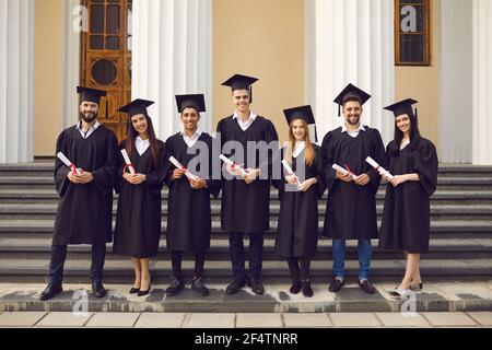 Gruppe von Absolventen in akademischen Kleidern posiert mit Diplomen gegen Der Hintergrund der Universität Stockfoto
