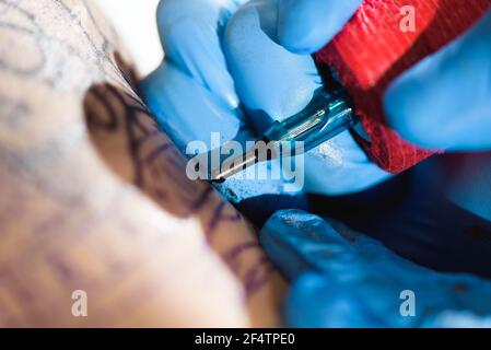Master Tattoo zeichnet die schwarze Farbe auf die Kunden Tattoo. Tattoo-Künstler hält eine Tattoo-Maschine in blauen sterilen Handschuhen und arbeitet an der Stockfoto